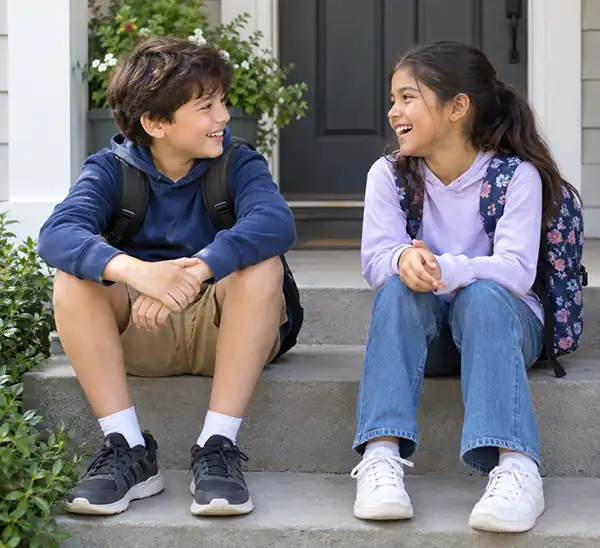 Two children sitting on a front step talking and laughing together after school