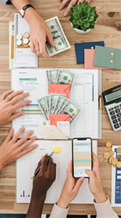 A hand hovering over a phone banking app next to a paper budget notebook, symbolizing the pull between impulse and planning