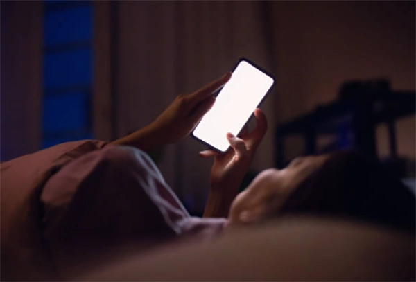 A person scrolling a shopping app late at night in a dimly lit room