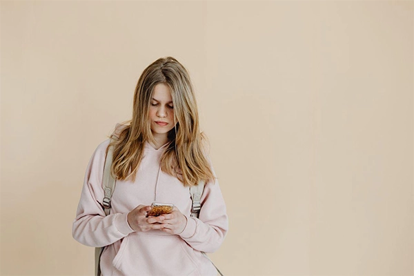 a teenage girl in a hoodie and backpack checking her smartphone